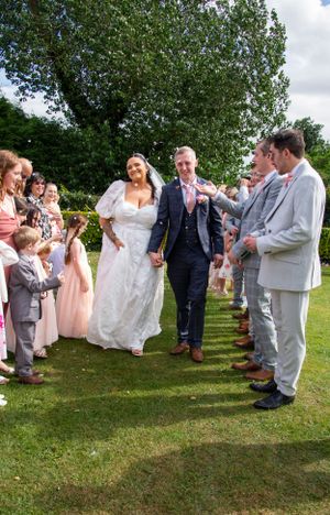 Wedding party walking through a guest-lined pathway on a grassy lawn.