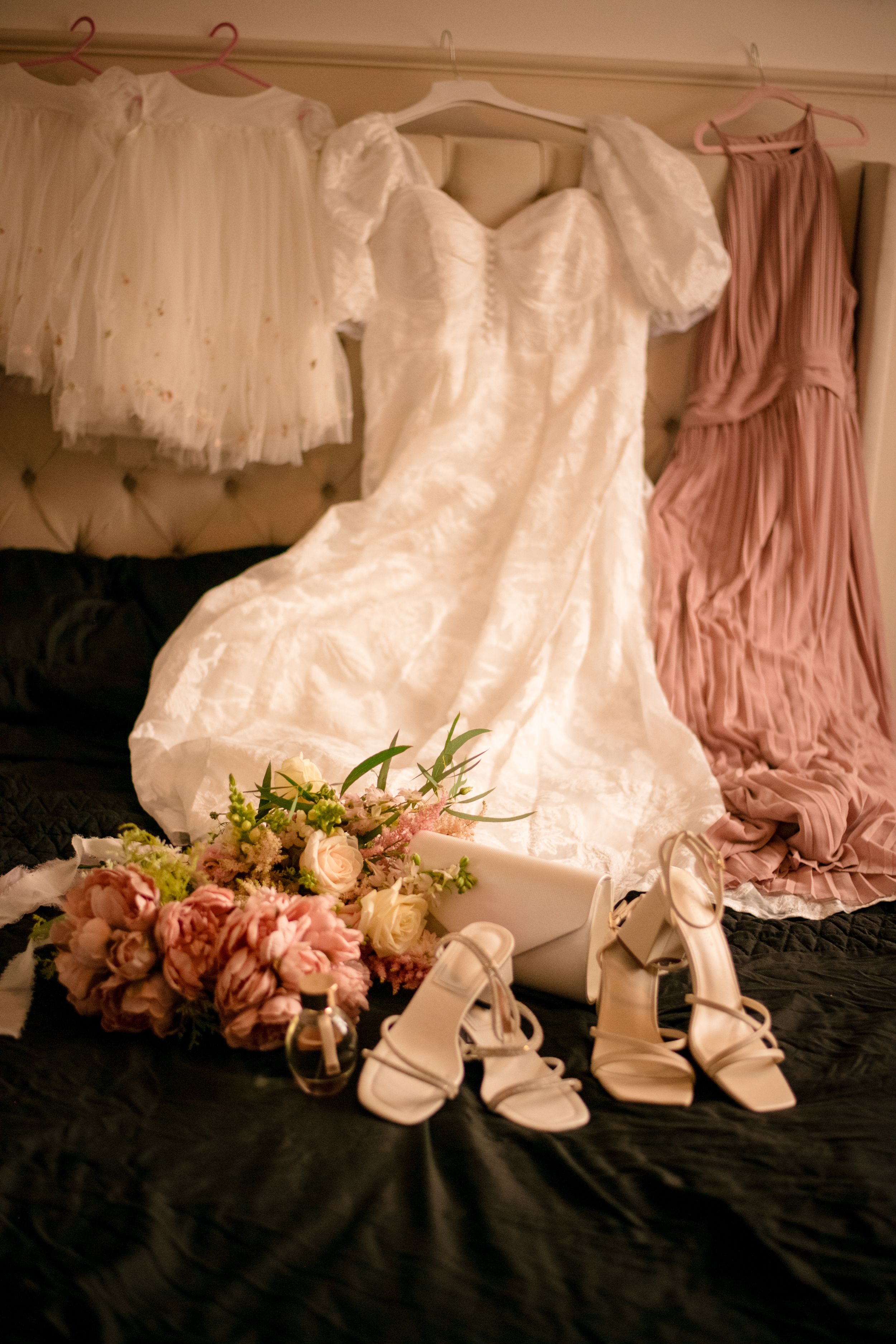 Wedding dress displayed with pink bridesmaid gown, bridal shoes and floral bouquet.