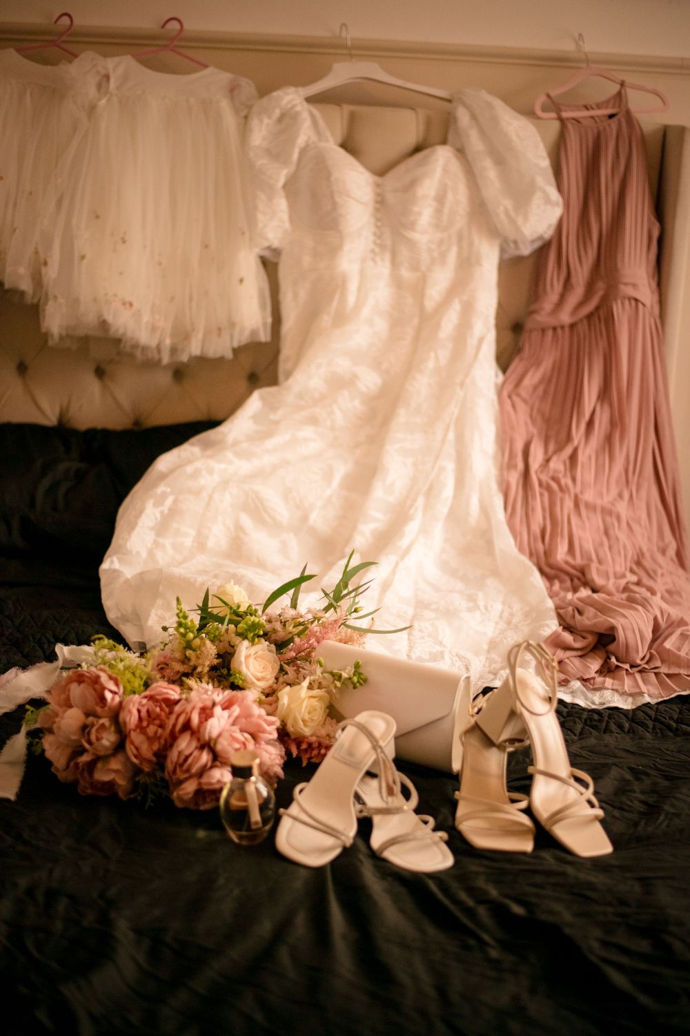 Wedding dress displayed with pink bridesmaid gown, bridal shoes and floral bouquet.