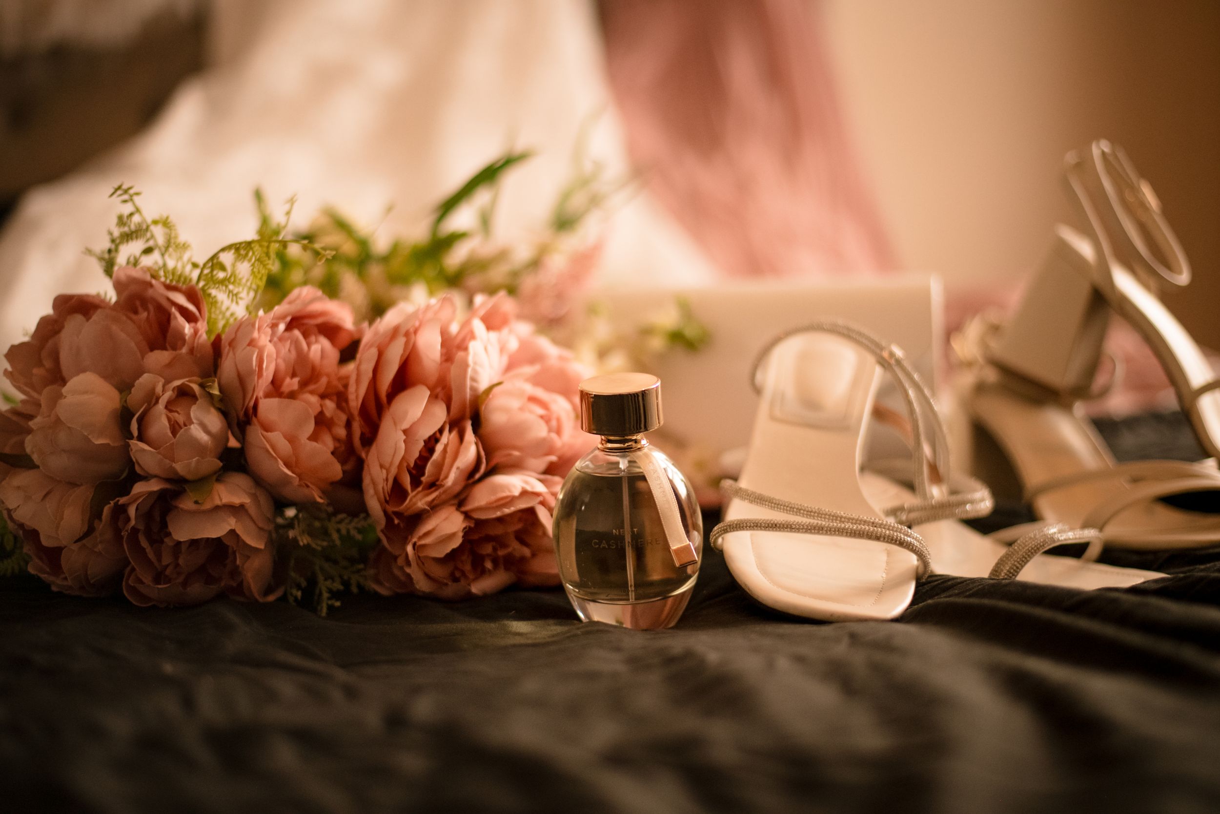 Pink roses and bridal shoes arranged elegantly in soft focus lighting.