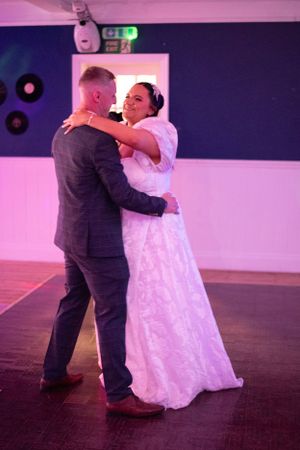 First dance at wedding reception with pink and purple lighting on dance floor.
