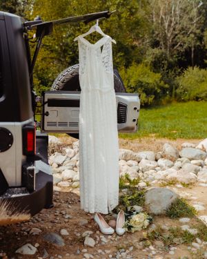 White lace wedding dress hanging from Jeep with bridal shoes beneath.