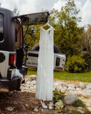 Elegant white wedding gown displayed on vehicle mirror in outdoor setting.