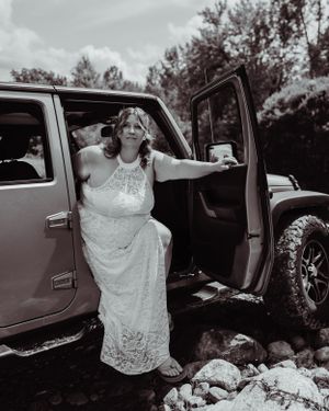 Black and white photo of person in wedding dress stepping out of Jeep.