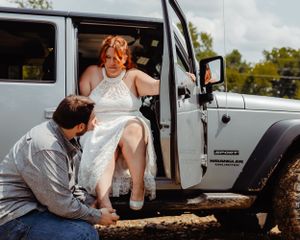 Wedding day moment of dress adjustment by silver Jeep outdoors.