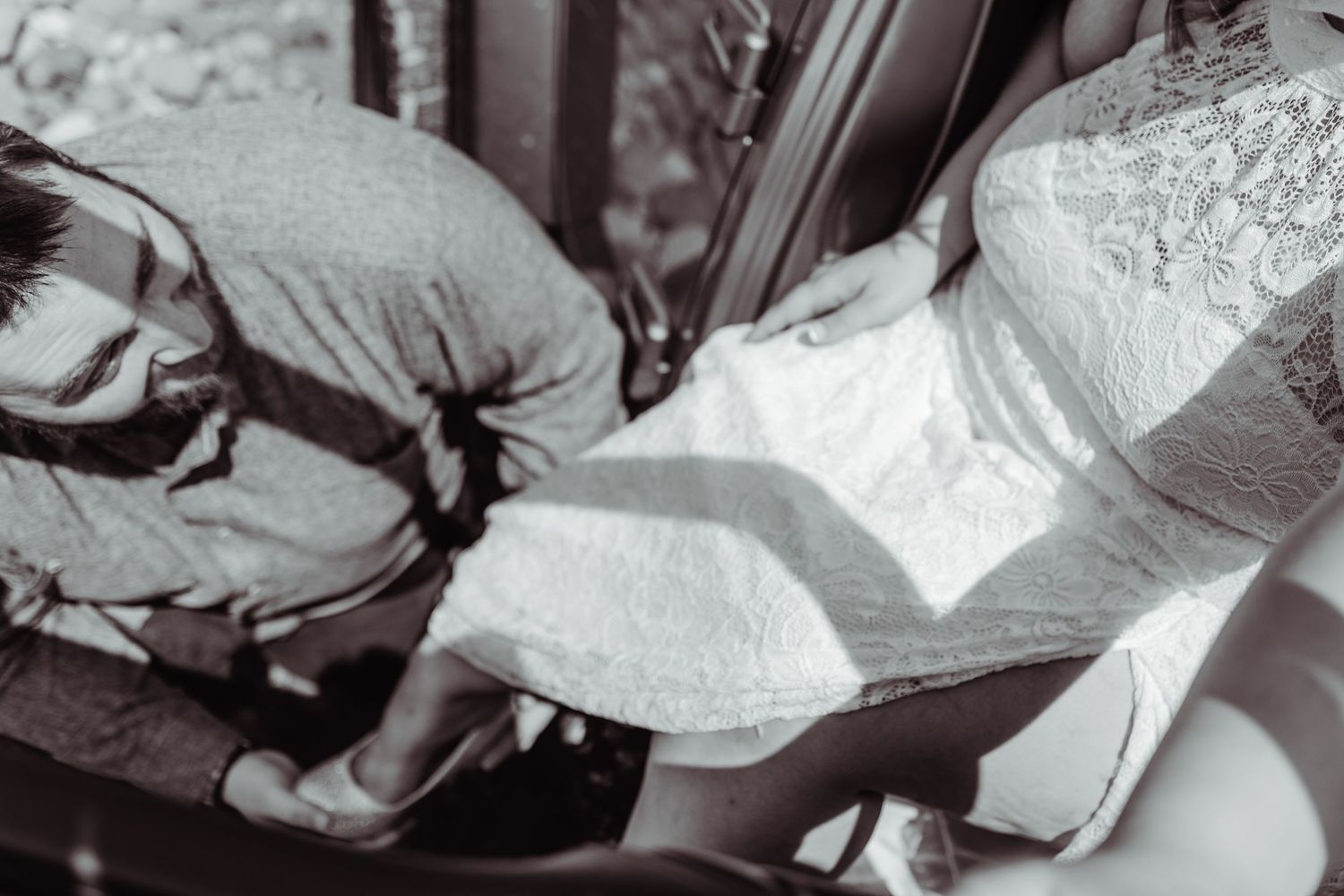 Black and white close-up of wedding dress detail by vehicle door.