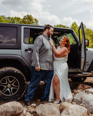 Romantic wedding photoshoot featuring newlyweds posing by their Jeep Wrangler on rocky ground.