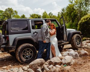 Wedding couple embraces near their grey Jeep Wrangler in outdoor setting.