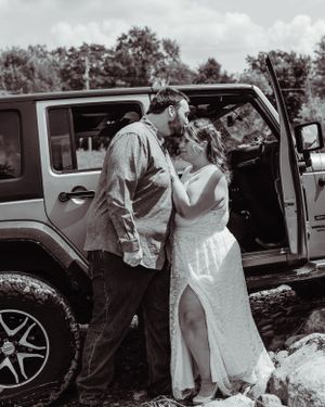 Black and white photo of newlyweds sharing tender moment by Jeep door.