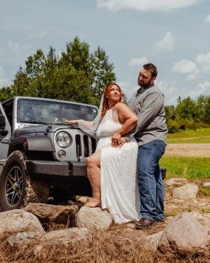 Couple poses together on rocky outcrop with grey Jeep Wrangler in background.