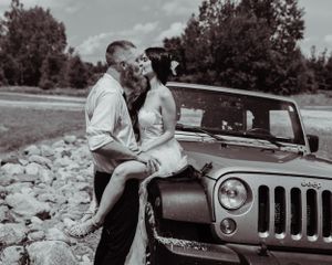 A romantic monochrome photo of a couple with their vintage Jeep parked on rocky terrain.