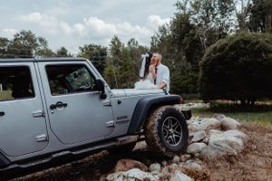A couple shares an intimate moment on their silver Jeep Wrangler during their wedding photoshoot.