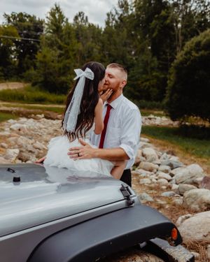 A couple embraces on top of their silver Jeep Wrangler during an outdoor wedding shoot.