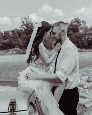 An intimate black and white portrait of a couple sharing a tender moment against their Jeep.