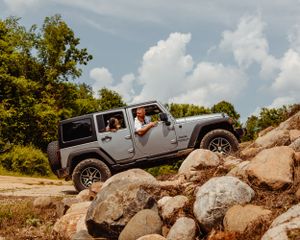 A silver Jeep Wrangler climbs over large boulders during an adventurous off-road session.