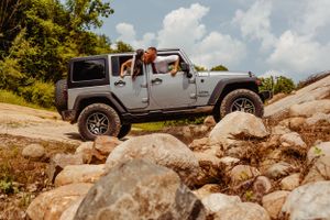 A silver Jeep Wrangler navigates rocky terrain during an outdoor photo shoot.