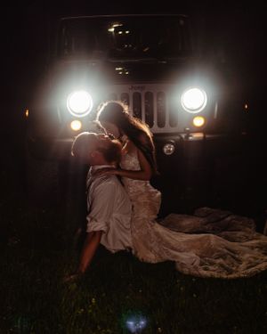 A romantic wedding portrait at night with a Jeep's bright headlights creating a dramatic silhouette.