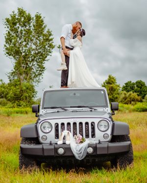 A dramatic wedding pose captured on top of a silver Jeep Wrangler in a lush field.
