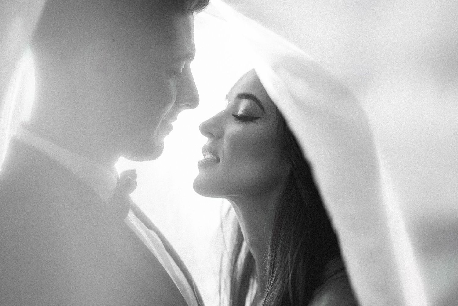 Intimate black and white portrait of a couple sharing a romantic moment under a veil.
