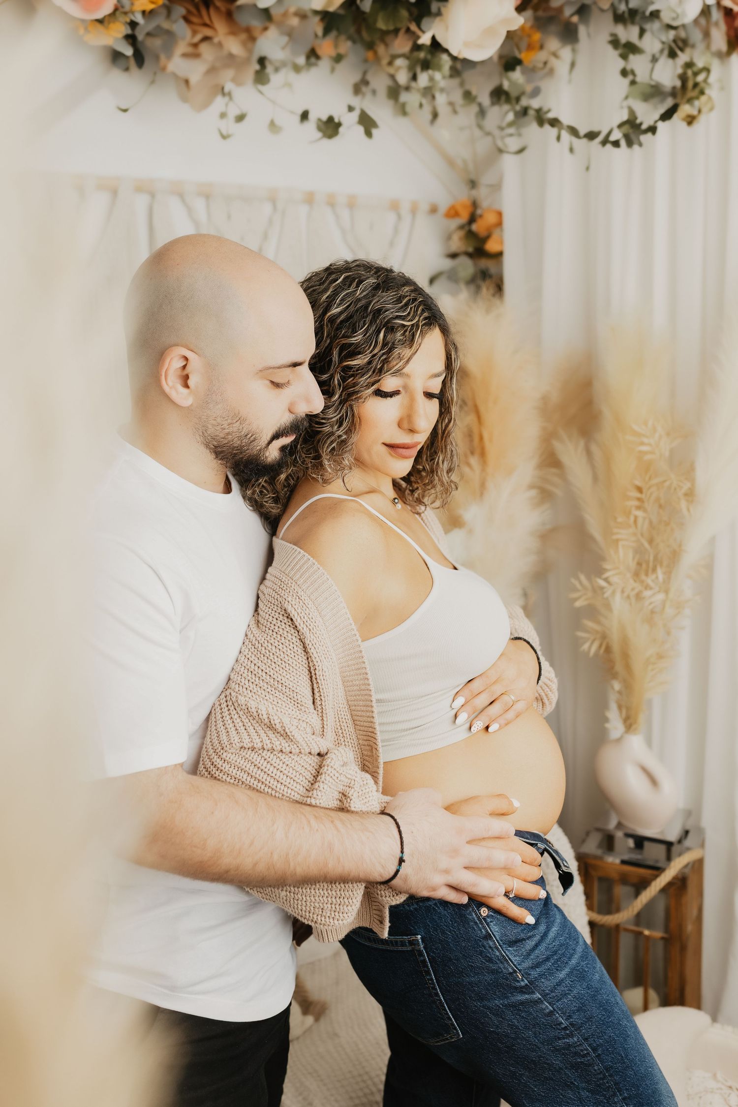 Intimate maternity portrait with couple embracing against floral backdrop.