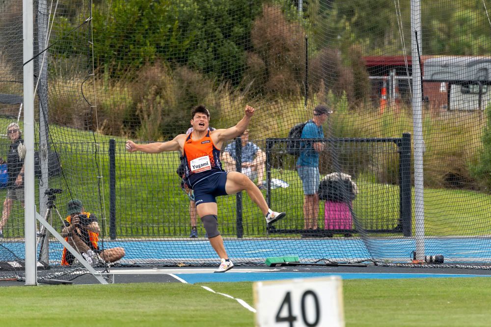 Athlete performs long jump at track and field competition on blue landing mat.