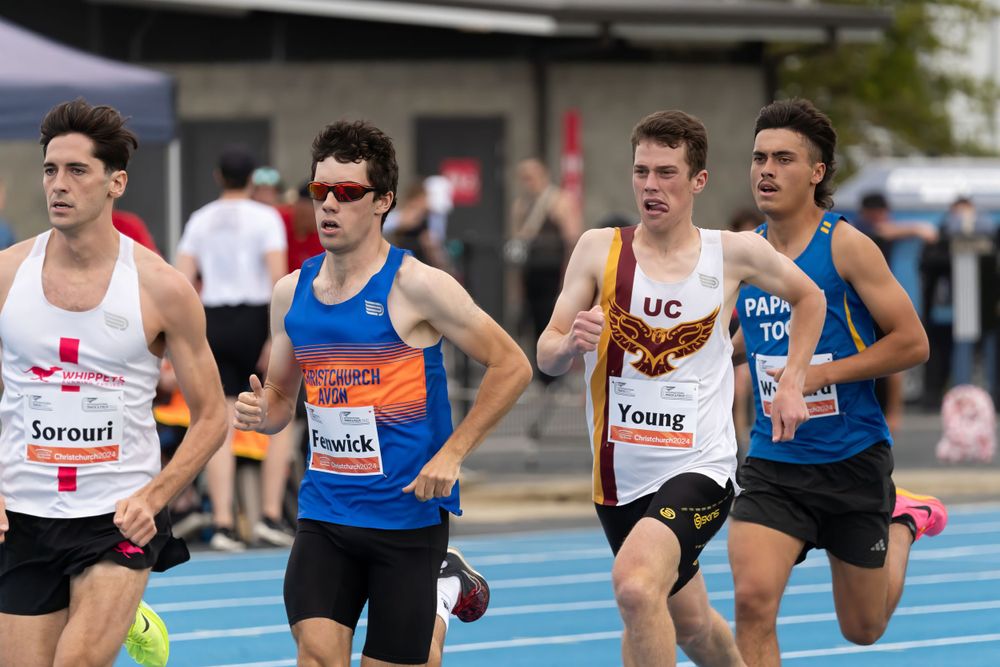 Group of runners competing in track race on blue running surface.