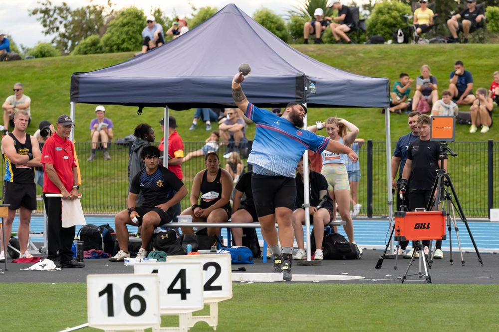 Athletes and spectators gather under tent during outdoor track meet.