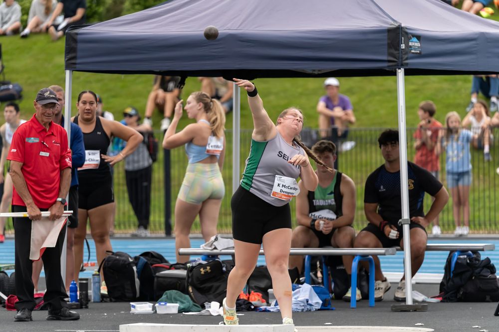 Athletes preparing for shot put competition under canopy tent at outdoor track meet.