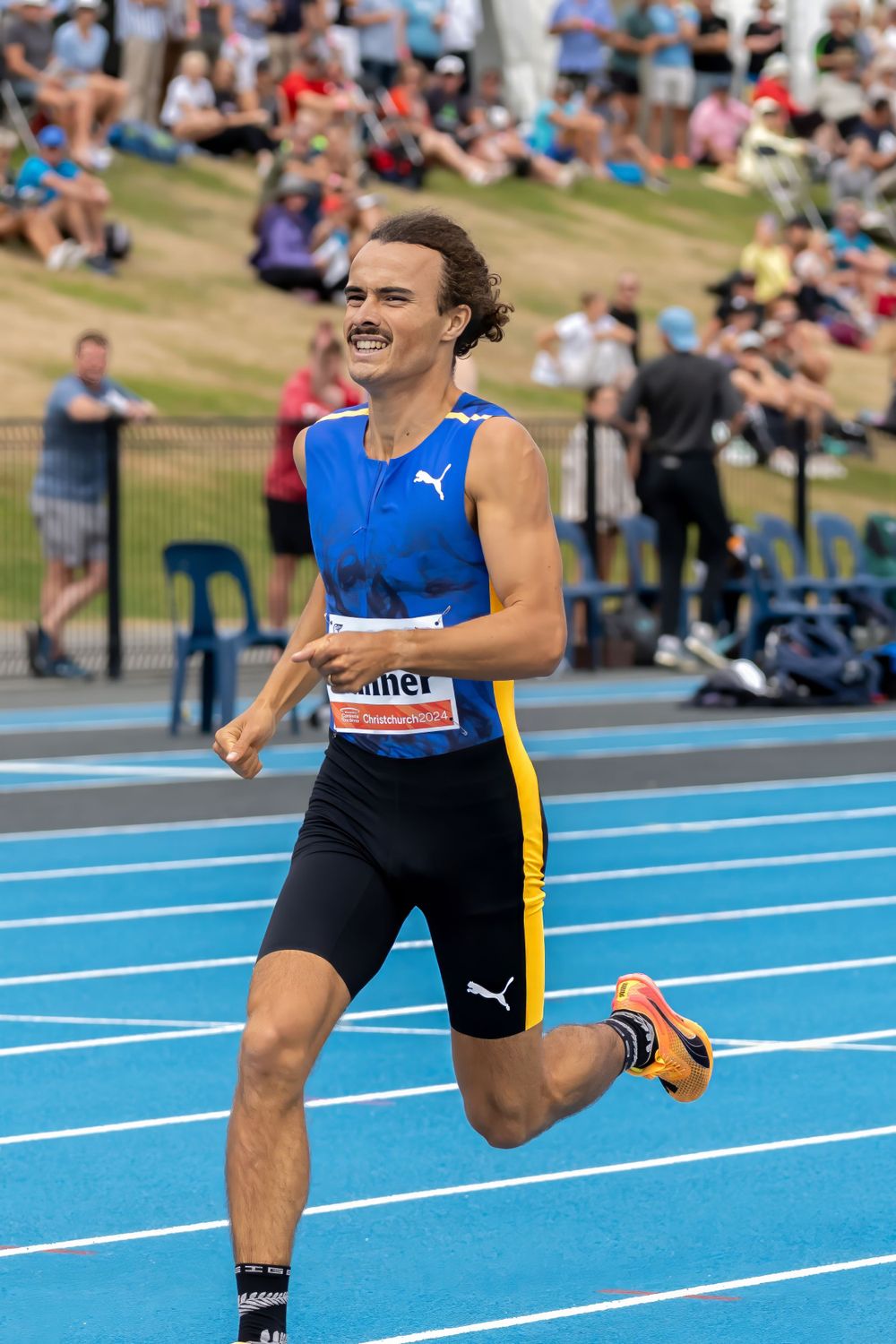 Athlete in blue singlet runs on outdoor track during competition.
