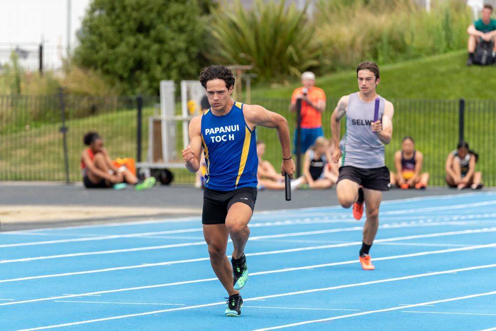 Athletes compete in a sprint race on a blue track during an outdoor competition.