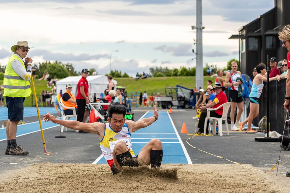 Athlete performing long jump landing in sand pit during track meet competition.