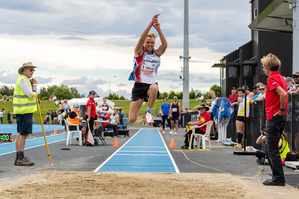 Athlete performing long jump with spectators watching from sidelines on cloudy day.