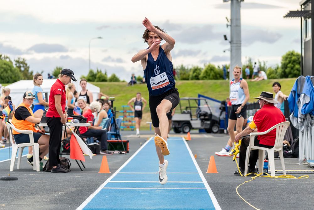 Track athlete in mid-air during long jump competition on outdoor blue runway.