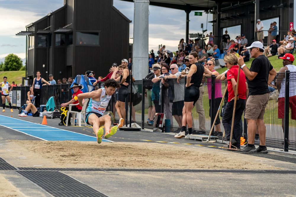 Competitor performing long jump with crowd watching from behind barrier.