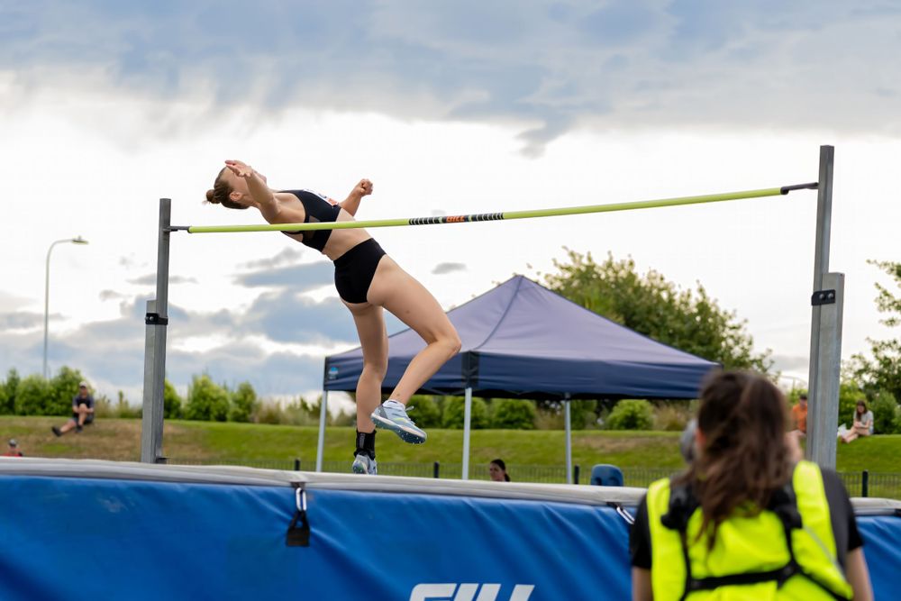 Athlete clearing high jump bar using Fosbury Flop technique at outdoor competition.