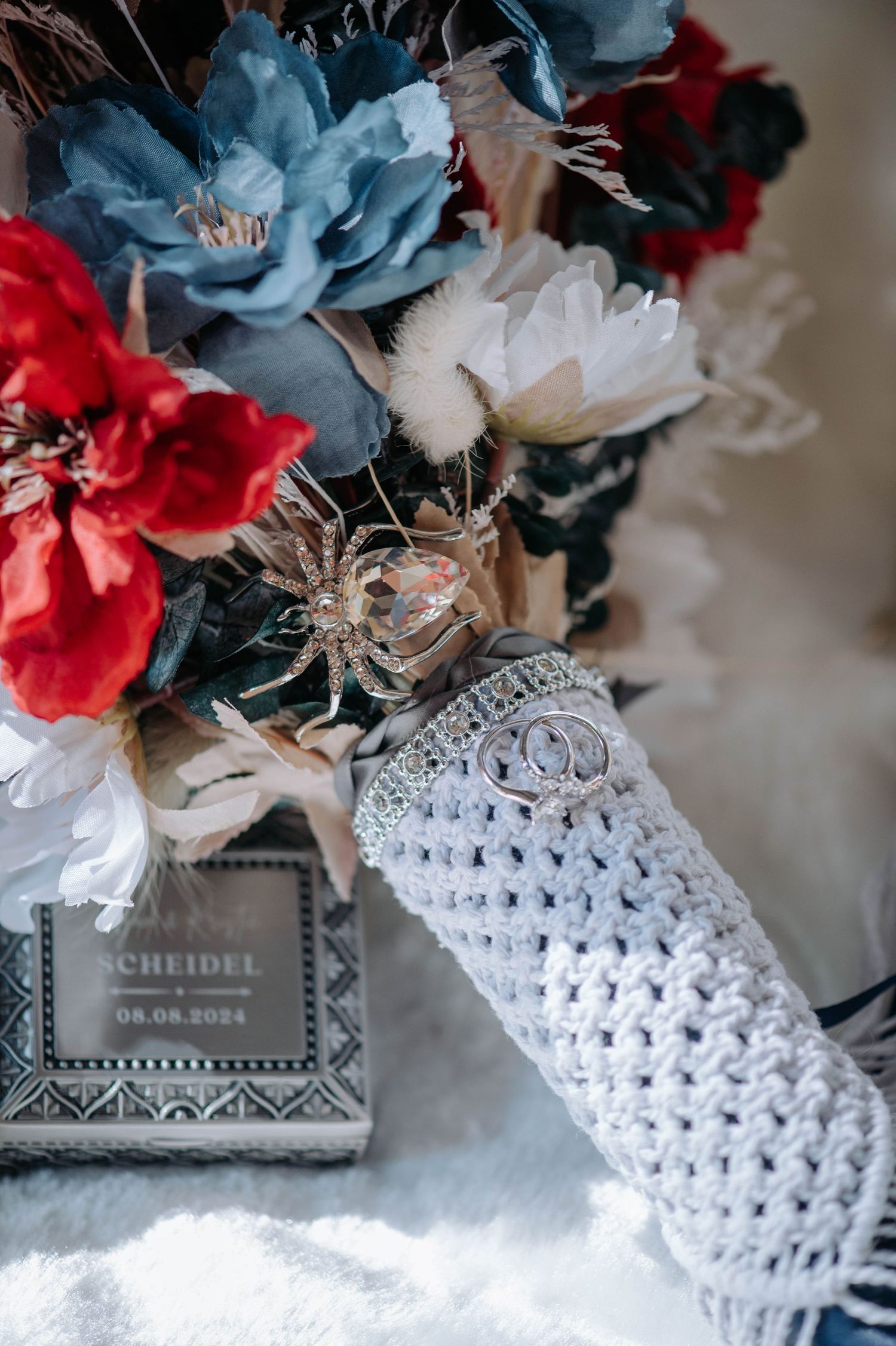 A wedding bouquet with blue and red flowers wrapped in white crochet fabric.