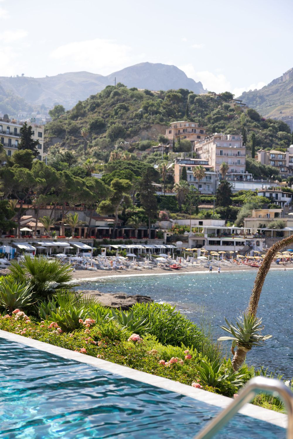 Infinity pool overlooking a coastal beach town with mountains in the background.