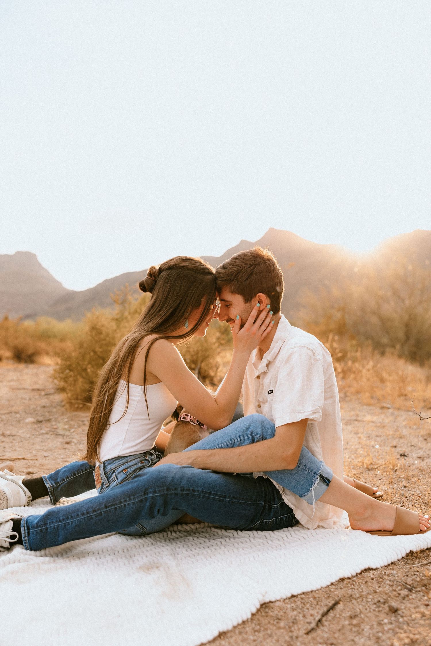 Intimate couple moment captured on blanket in desert setting during golden hour.