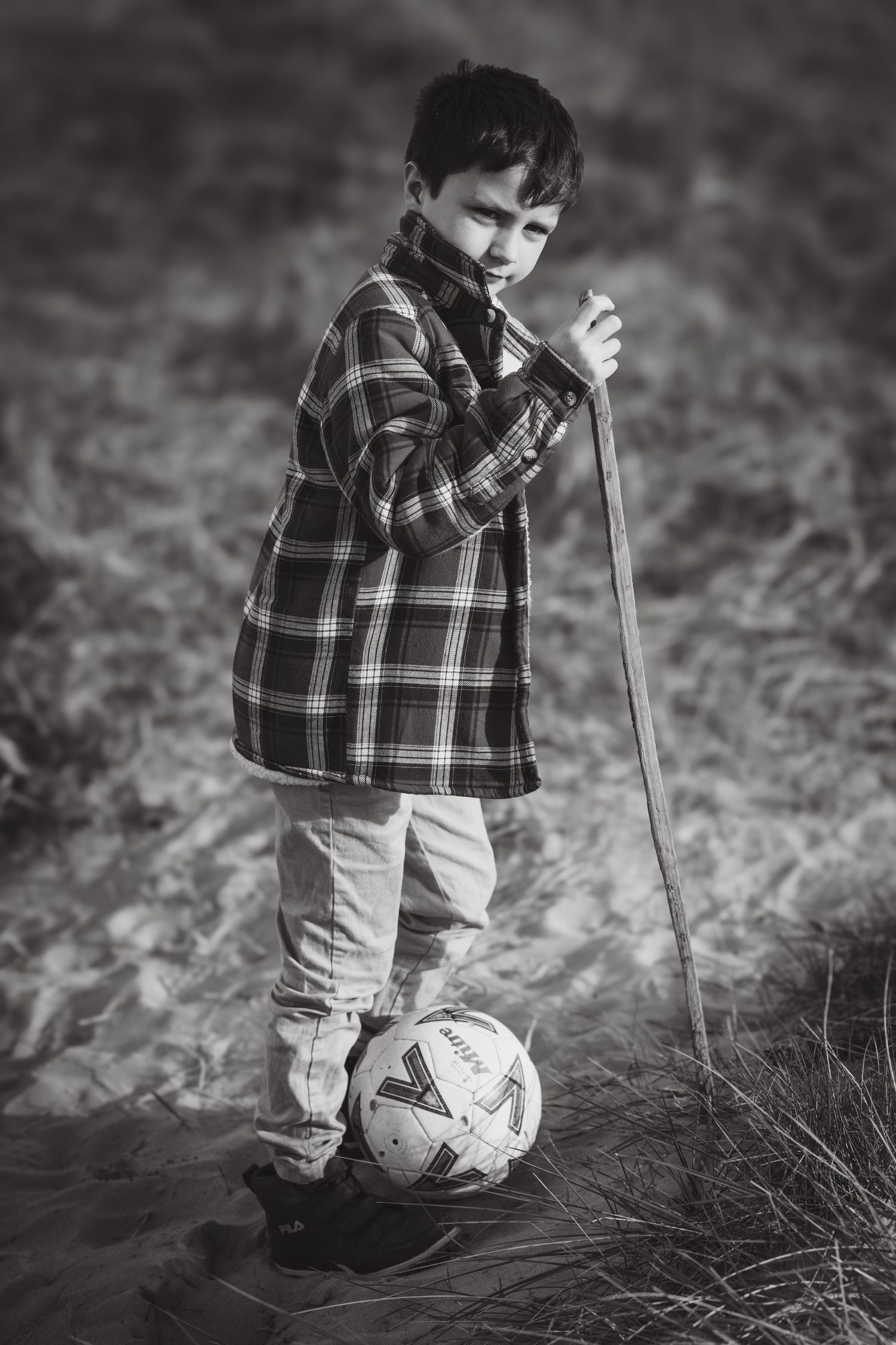 Black and white portrait in plaid jacket with walking stick and soccer ball.