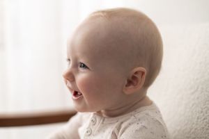 Smiling baby with light hair wearing a white onesie, captured in a soft, bright portrait photo birthday photoshoot Nottingham