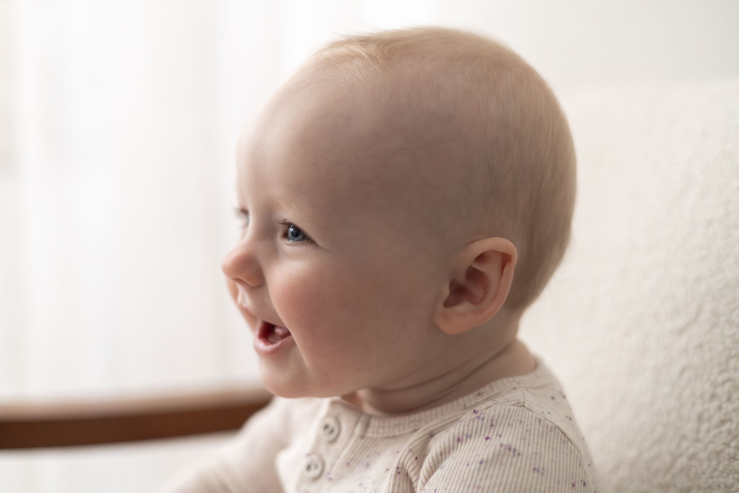 Smiling baby with light hair wearing a white onesie, captured in a soft, bright portrait photo birthday photoshoot Nottingham