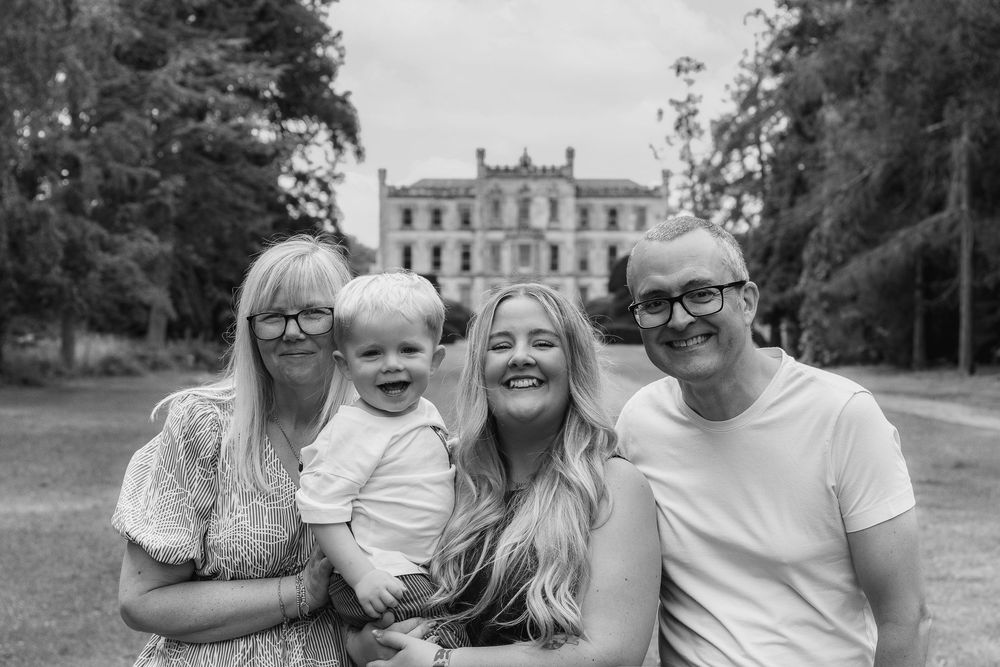 Black and white family portrait of f3 generations smiling outdoors with a grand manor in the background Outdoor family photoshoot Nottingham