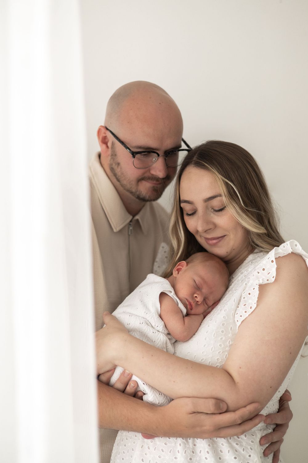Parents tenderly holds their sleeping newborn baby,  against a soft white background Nottingham Newborn photographer