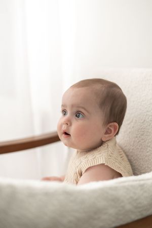 Adorable baby with blue eyes sitting in a white chair looking up curiously milestone birthday photoshoot Nottingham photographer