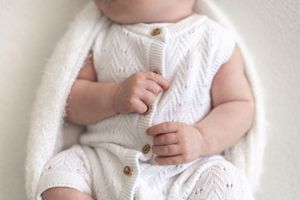 Close-up of a baby in a white knit romper with wooden buttons, tiny hands clasped together natural newborn photoshoot Nottingham