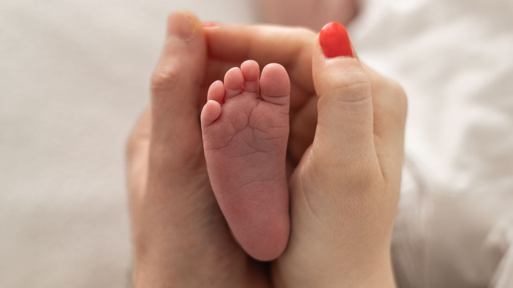 Close-up of a mother and fathers hands gently cradling a newborn baby's tiny foot, natural newborn photoshoot Nottingham