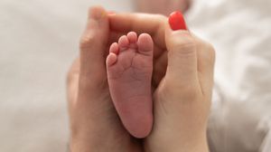 Close-up of a mother and fathers hands gently cradling a newborn baby's tiny foot, natural newborn photoshoot Nottingham
