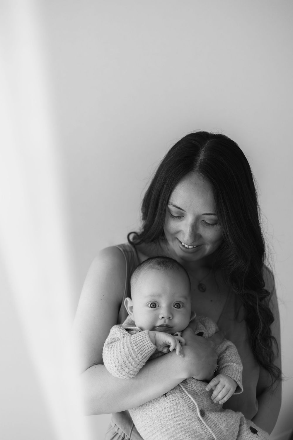 Black and white photo of a smiling mother tenderly holding her newborn baby against a light background natural newborn photoshoot Nottingham