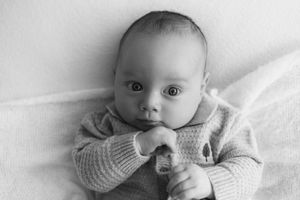 Black and white portrait of a newborn baby lying on a soft blanket, gazing at the camera with hands near chin newborn photoshoot Nottingham