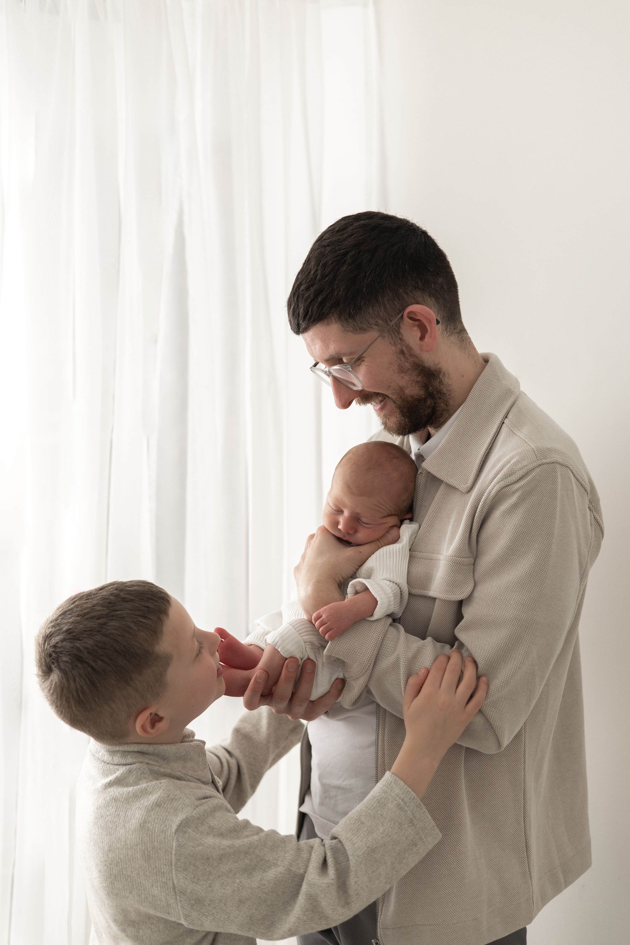 Newborn photographer Nottingham cosy home studio Father holds newborn baby while young son gently touches infant's foot